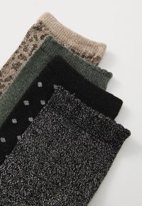 Cuatro pares de calcetines en diferentes tonalidades: beige con brillo, verde, negro con lunares blancos y negro brillante, mostrando diversas texturas.