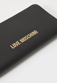 Črna denarnica iz teksturiranega materiala z zlatim logotipom "LOVE MOSCHINO" na sprednji strani, z zadrgo in zaobljenimi koti.