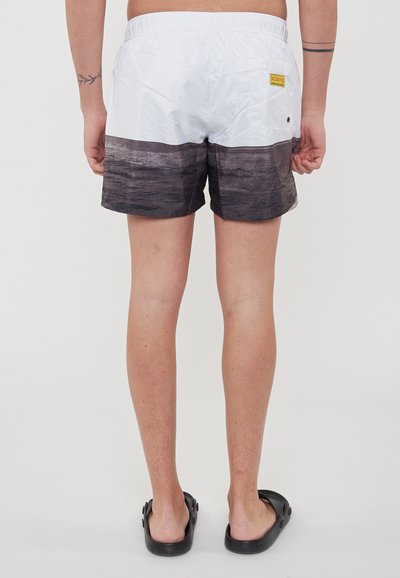 Shorts da bagno bianchi con un motivo d'acqua grigio scuro nella parte bassa. Presentano un elastico in vita e un'etichetta della marca gialla.