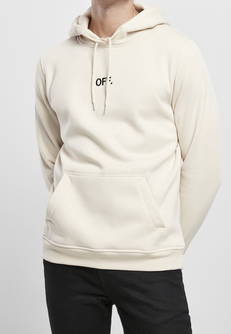 Sweat à capuche beige avec une poche kangourou à l'avant et une capuche à cordon. Présente le texte "OFF." en noir, fabriqué en tissu doux.