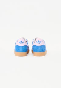 Sneaker in suede blu erosa con suola in gomma, tre accenti a striscia rosa e un tassello al tallone rosa con il logo Adidas.