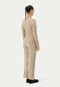 Beige ribbat stickad topp och byxset, med långa ärmar och en figurnära silhuett. Mjuk textur med vertikala ränder, kombinerad med svarta skor.