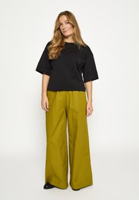 Mustast lühikeste varrukatega lühendatud t-särk, mis on kombineeritud laia säärega oliivroheliste pükstega. Mõlemal riideesemel on sile tekstuur ja lõdvestunud istuvus.