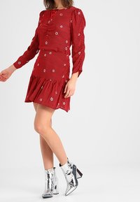 Rot gestreiftes Kleid mit langen Ärmeln, verziert mit Sternstickerei und einem ausgestellten Saum. Kombiniert mit glänzenden silbernen Stiefeletten mit Blockabsätzen.