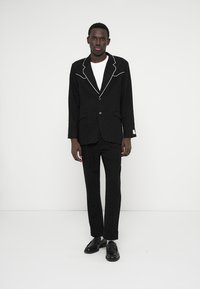 Fato preto com um padrão texturizado, featuring um colarinho branco a condizer, fecho de um único botão e calças slim-fit a condizer. Sapatos pretos incluídos.