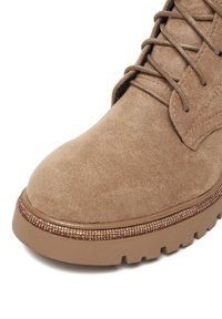 Gheată ankle din piele întoarsă maro deschis, cu vârf rotund, design cu șireturi și talpă din cauciuc texturată, decorată cu un accent de rhinestone pe margine.