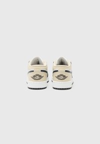 Zapatillas de cuero beige con suela blanca y acentos negros. En la parte posterior, se muestra un logo con un diseño de baloncesto alado.