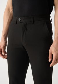 Černé kalhoty z hladké látky, úzkého střihu, s jediným knoflíkem a bočními kapsami. Minimalistický styl bez viditelných vzorů.