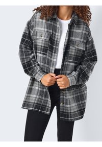 Koszula flanelowa w czarno-szary kratę, z zapięciem na guziki z przodu, kieszeniami na piersi i luźnym krojem. Widoczny strukturalny materiał.