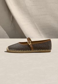 Καφέ επίπεδο εσπαντρίγια με υφή, ταμπά περίγραμμα, πλευρικό λουράκι με χρυσή αγκράφα και ραμμένη σόλα από τζούτ σε ουδέτερο φόντο.