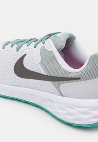 Nike löparsko med vit mesh-ovandel och grå detaljer, en texturerad grå Swoosh och en turkos sula. Inkluderar ljusgrå skosnören.