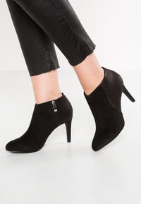 Botines negros de ante con punta afilada y tacón texturizado. Presentan una cremallera lateral y material superior suave.