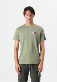 Olive green cotton t-shirt with short sleeves and a crew neck, featuring a small stitched logo in red, white, and blue on the left chest.