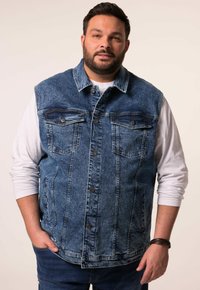 Denimová vesta ve středně modré barvě, s knoflíkovou přední částí, dvěma kapsami na hrudi a postranními kapsami. Nositá přes bílou dlouhou rukávovou košili.