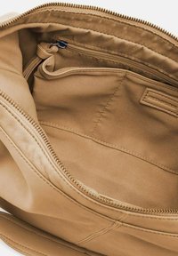 Interno di una borsa a tracolla in pelle beige con una texture liscia, dotato di una tasca con zip e un'etichetta intrecciata. Le cuciture sono pulite e ben strutturate.