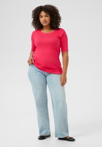 Top ajustado de color rosa con mangas cortas y escote redondo, combinado con jeans rectos de color azul claro y zapatos planos negros. Tejido de textura suave.