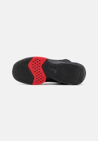Semelle de chaussure de basketball avec une base en caoutchouc noir, des motifs texturés et un accent rouge en forme de diamant près du centre.