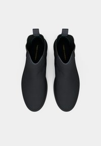 Par et par sorte slip-on sko med pull-tabs, ribbet ankelkrave og "Tommy Hilfiger" branding indeni, vist fra oven på en hvid baggrund.