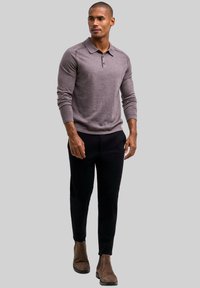 Jasnobrązowy sweter polo z kołnierzykiem, długimi rękawami i dwoma guzikami, w połączeniu z czarnymi, eleganckimi spodniami i brązowymi botkami za kostkę.