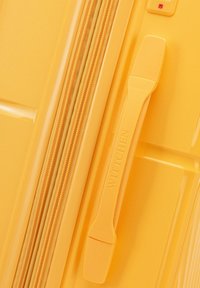 Maleta amarilla de carcasa dura con superficie texturizada, cierre de cremallera y asa con marca. Presenta un diseño ergonómico y material duradero.
