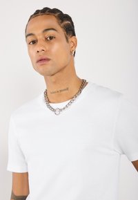 Hvid ribbet kortærmet T-shirt med rund halsudskæring, parret med et tykt sølv kædehalssmykke med en circular vedhæng.