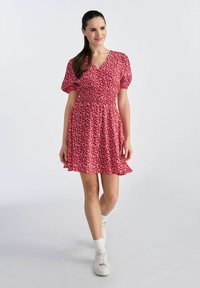 Czerwona sukienka w kwiaty z krótkimi bufkami i dopasowaną górą, z rozkloszowanym dołem. Wykonana z lekkiego materiału z delikatnym wzorem.