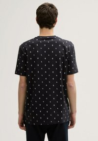 Camiseta negra de manga corta con un patrón floral blanco repetido, confeccionada con un tejido suave y con un cuello redondo clásico.