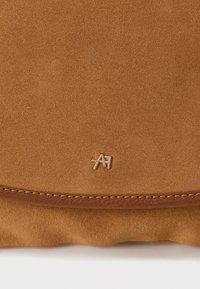 Brown suede handbag featuring a smooth leather border, gold hardware logo, and a soft, textured surface.