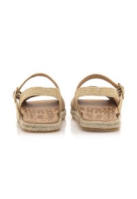 Sandalias de esparto con correas de paja trenzada, color beis, suelas planas y suelos de goma con un patrón en relieve. Detalle de hebilla en las correas.