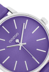 Purple watch with a matte dial, silver hour markers, and hands. Metal case and a purple strap. Logo "oozoo" displayed on the dial.