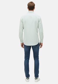 Camisa a rayas verde claro con cuello, cierre de botones y mangas largas, combinada con jeans azul oscuro y zapatillas blancas.