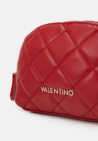 Crvena quilted kožna torbica s zlatnim "Valentino" logotipom, zaobljenog oblika i glatke teksture s istaknutim šavovima u dijamantnom uzorku.