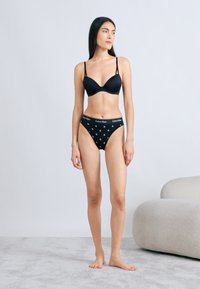 Μαύρο σουτιέν Calvin Klein με ρυθμιζόμενους ιμάντες και μαύρο εσώρουχο που ταιριάζει με διακριτικό σχέδιο καρδιάς. Λείο ύφασμα, ελαφρύ σχέδιο.