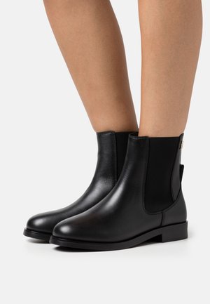Botas de cuero negro hasta el tobillo con paneles laterales elásticos, punta redonda y suela plana. Textura suave con un diseño minimalista y sin hardware visible.