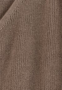 Gros plan d'un tissu tricoté marron montrant un motif côtelé vertical et des points texturés avec une couture pliée en haut à gauche.