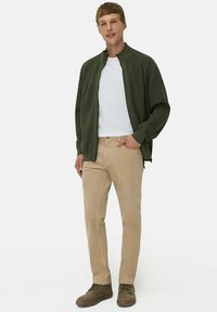 Grüne Zip-Jacke über einem weißen T-Shirt, kombiniert mit beigen Hosen und grünen Stiefeln. Glatte Texturen und lässiges Design.