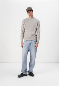 Grauer, gestrickter Pullover mit geripptem Saum, kombiniert mit lockeren, hellblauen Jeans. Stylt mit einer karierten Mütze und schwarzen Schuhen. Minimalistischer Hintergrund.