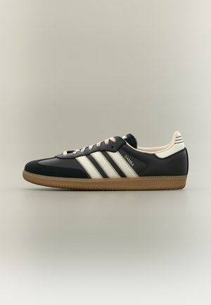Schwarzer Adidas Samba Sneaker mit weißen Streifen, beigen Schnürsenkeln und Gummisohle, seitlich auf neutralem Hintergrund dargestellt.
