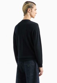 Maglione nero a maglia con un motivo a spina di pesce testurizzato, colletto rotondo e polsini a coste, abbinato a pantaloni in denim scuri.