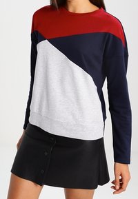 Sudadera de manga larga en bloques de color con paneles en rojo, marino y gris; cuello redondo; tejido suave; combinada con una falda de cuero sintético negra.