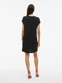 Robe noire courte avec des manches retroussées, coupe décontractée et ourlet arrondi. Associée à des talons rouges à lanières, mettant en valeur la texture du tissu lisse.