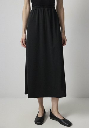 Čierna maxi sukňa vyrobená z jemného materiálu, s elastickým pásom a voľným siluetom. Skombinovaná s čiernymi plochými topánkami.