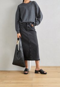 Donkergrijze sweatshirt met reliëftekst, gecombineerd met een lange zwarte denimrok, zwarte muiltjes en een zwarte leren tote bag met gouden hardware.