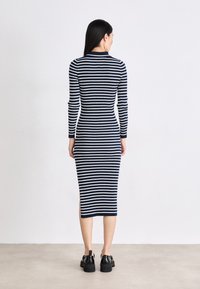 Šaty bodycon s dlhými rukávmi, námornícke a biele pruhy, ribbovaná textúra, dĺžka po polovicu lýtok, postranné rozparky, skombinované s čiernymi robustnými topánkami.