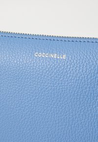 Portafoglio in pelle texture blu con chiusura a zip e logo stampato "Coccinelle" in oro.