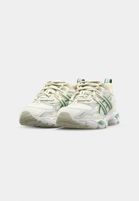 Baskets blanches avec des accents verts, présentant un dessus en mesh et en matière synthétique, une semelle texturée et un système de laçage proéminent. Conception à bout arrondi.