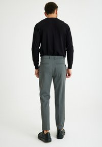 Grijze op maat gemaakte broek met een subtiele ruitpatroon, voorzien van twee achterzakken, gecombineerd met een zwarte lange mouwen top en zwarte sneakers.