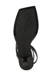 Sorte højhælede sandaler med en tekstureret sål med zigzag-mønster. Skoene har tynde remme og en lynlås bagpå til lukning.