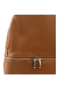 Sac à dos en cuir marron texturé avec une fermeture éclair argentée et des tirettes de fermeture éclair doubles. La surface présente un léger motif de grain.