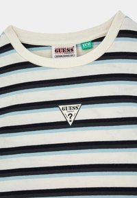 Gestreept T-shirt in wit, blauw en zwart. Heeft een ronde hals, zachte katoenstof en een driehoekig logo patch met "GUESS®".
